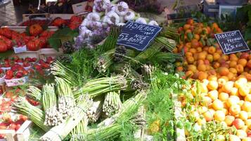 Un puesto de mercado con diversos productos frescos, incluyendo espárragos, tomates y albaricoques.