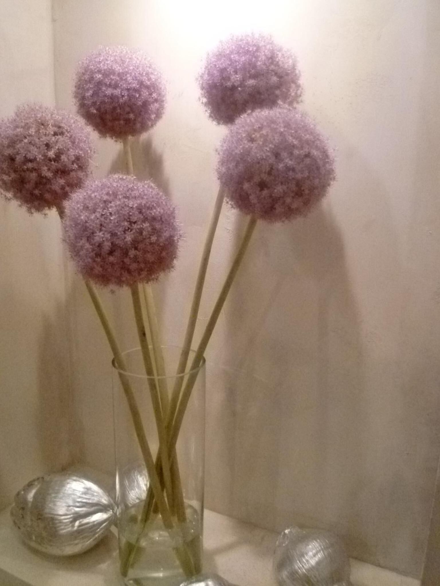 A clear glass vase with several stems and purple spherical flowers.