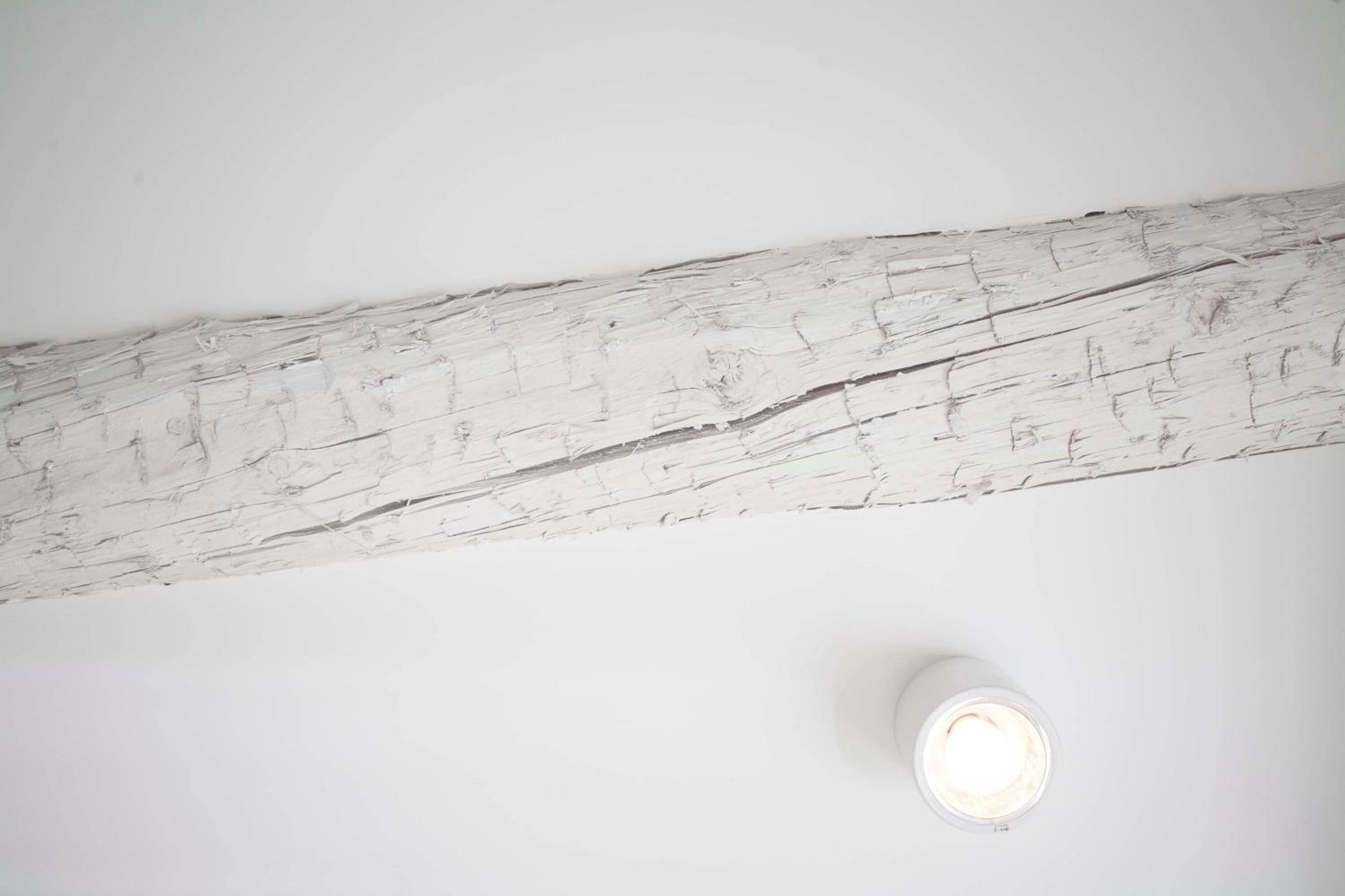 A white wall with a rustic wooden beam and a white cylindrical object.