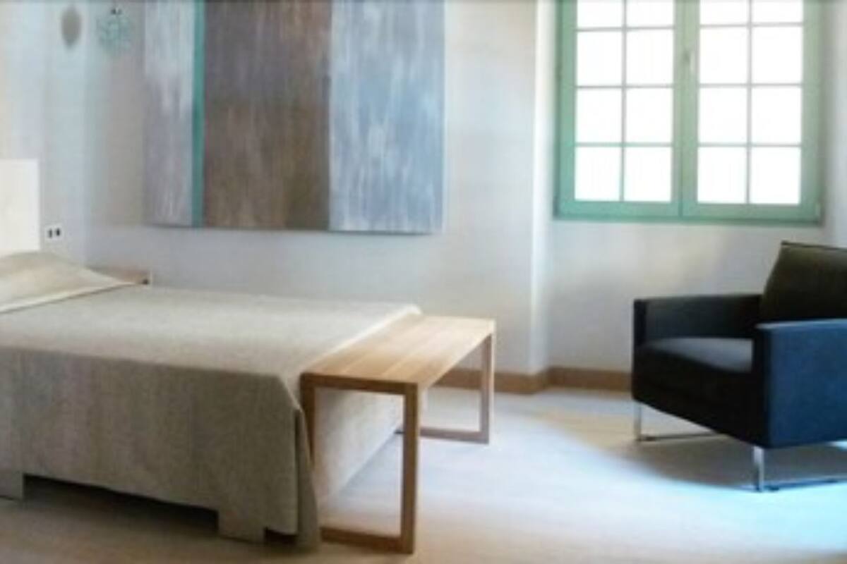 Un dormitorio con cama, mesita de noche, una silla y un cuadro en la pared.