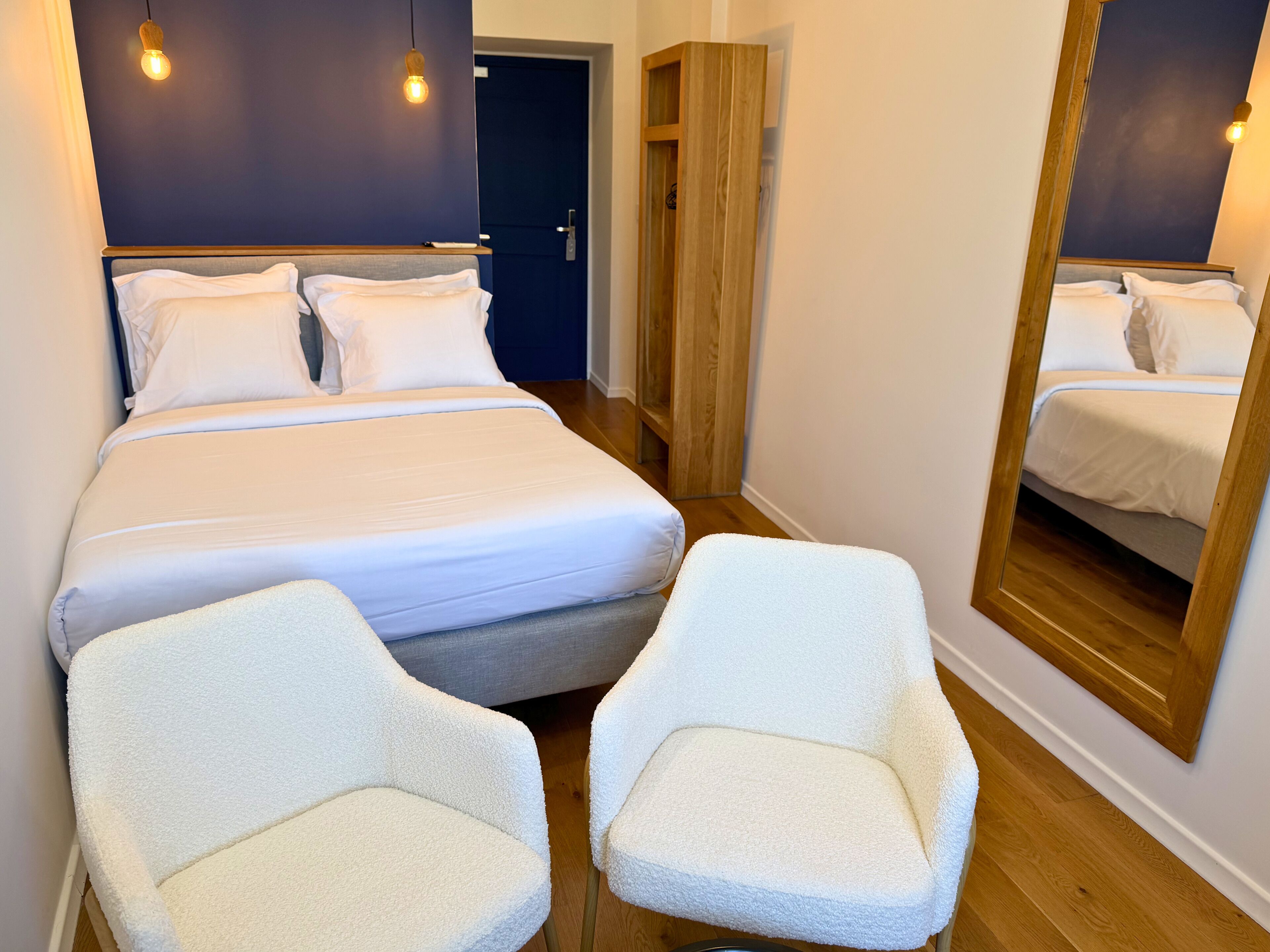 Un dormitorio ordenado con una cama, dos sillas, un espejo y una puerta.