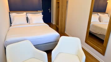 Un dormitorio ordenado con una cama, dos sillas, un espejo y una puerta.