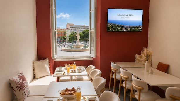 Desayuno preparado con mesas, sillas y vistas a un paisaje urbano a través de una ventana.