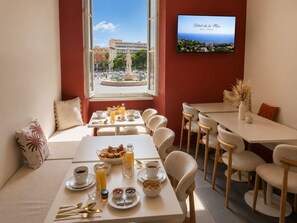 A breakfast setup with tables, chairs, and a view of a cityscape through a window. - Hotel De La Mer (Nice)