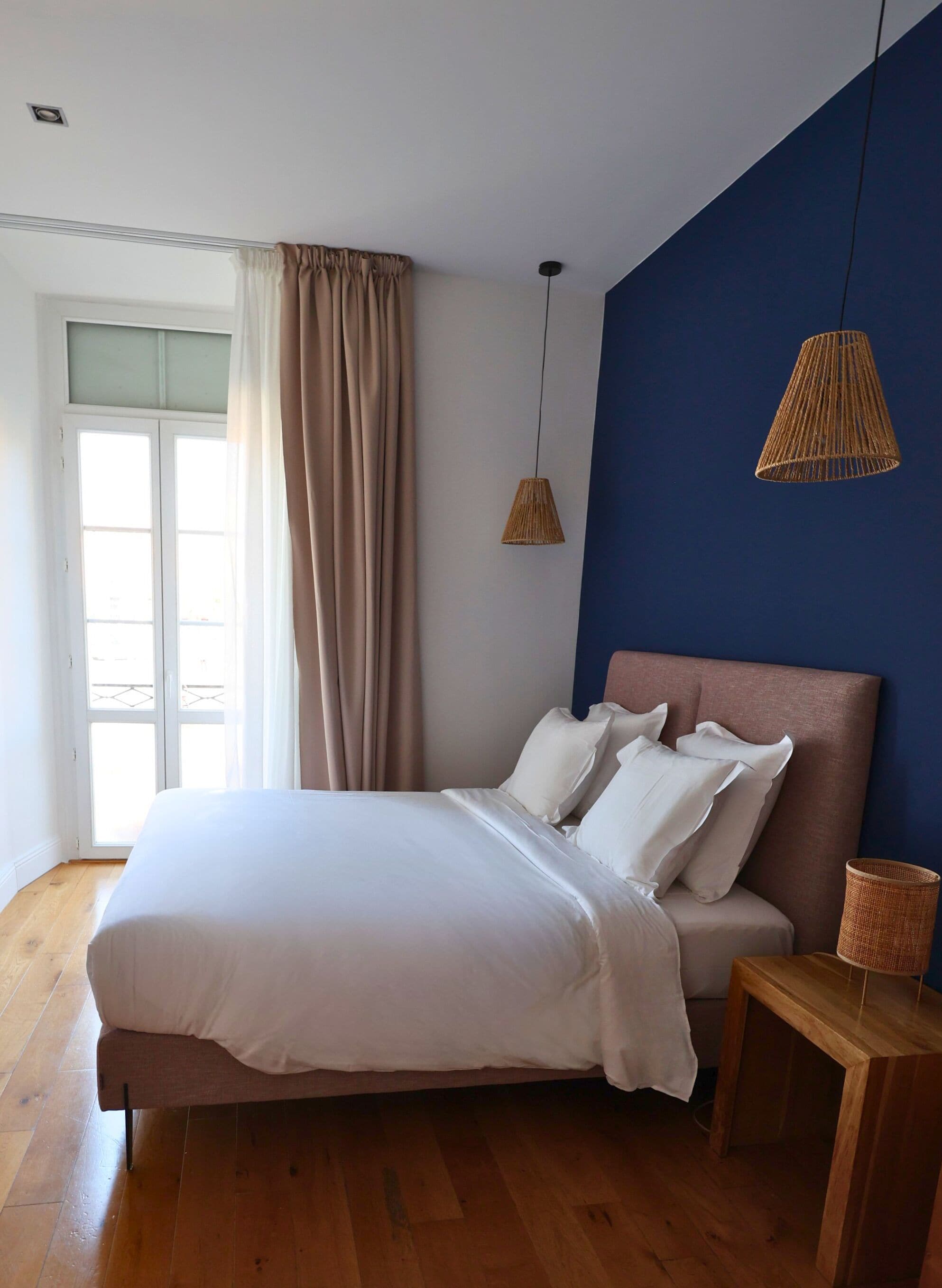 Un dormitorio con cama, mesita de noche, lámpara colgante y ventana con cortinas.