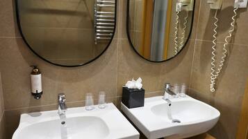 Baño con dos lavamanos, un espejo, toallero y secador de pelo.