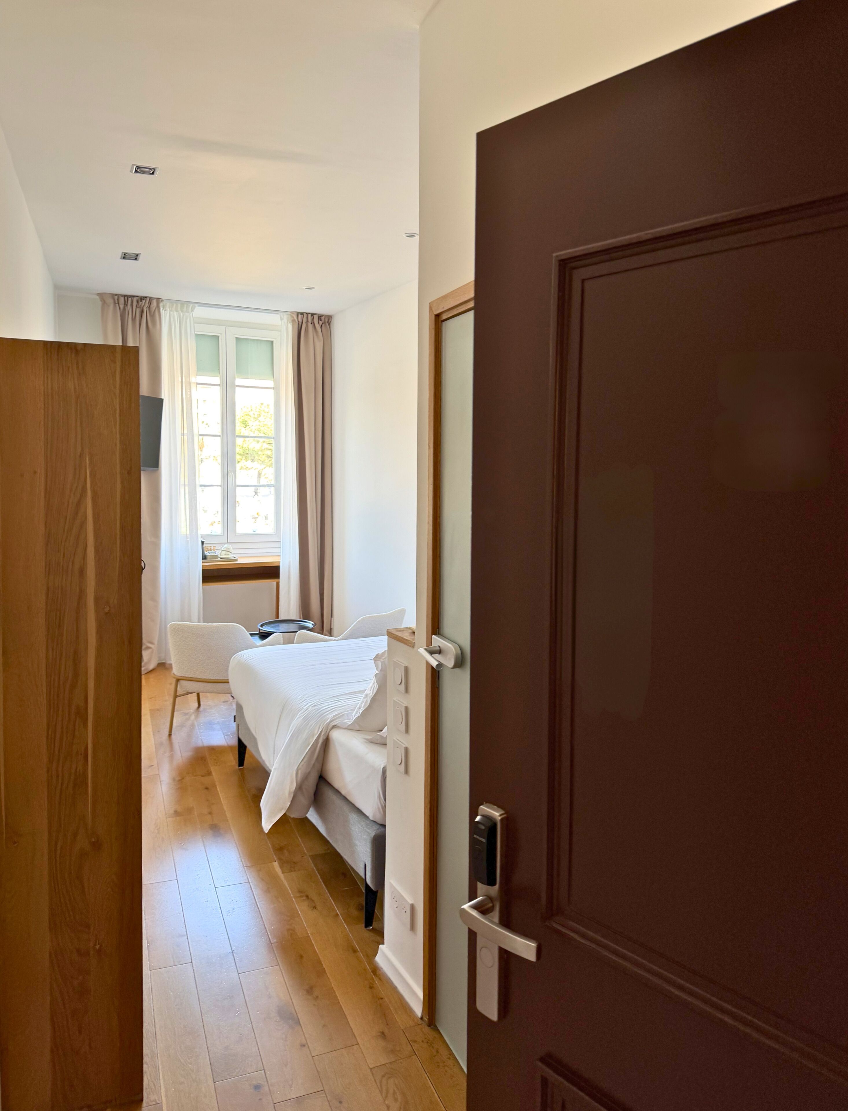 Un dormitorio con cama, ventana con cortinas, puerta de madera y suelo de madera.