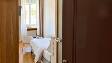 Un dormitorio con cama, ventana con cortinas, puerta de madera y suelo de madera.
