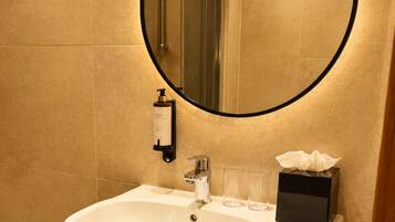A bathroom with a white sink, a mirror with a black frame, a towel rack, and a small shelf with toiletries.