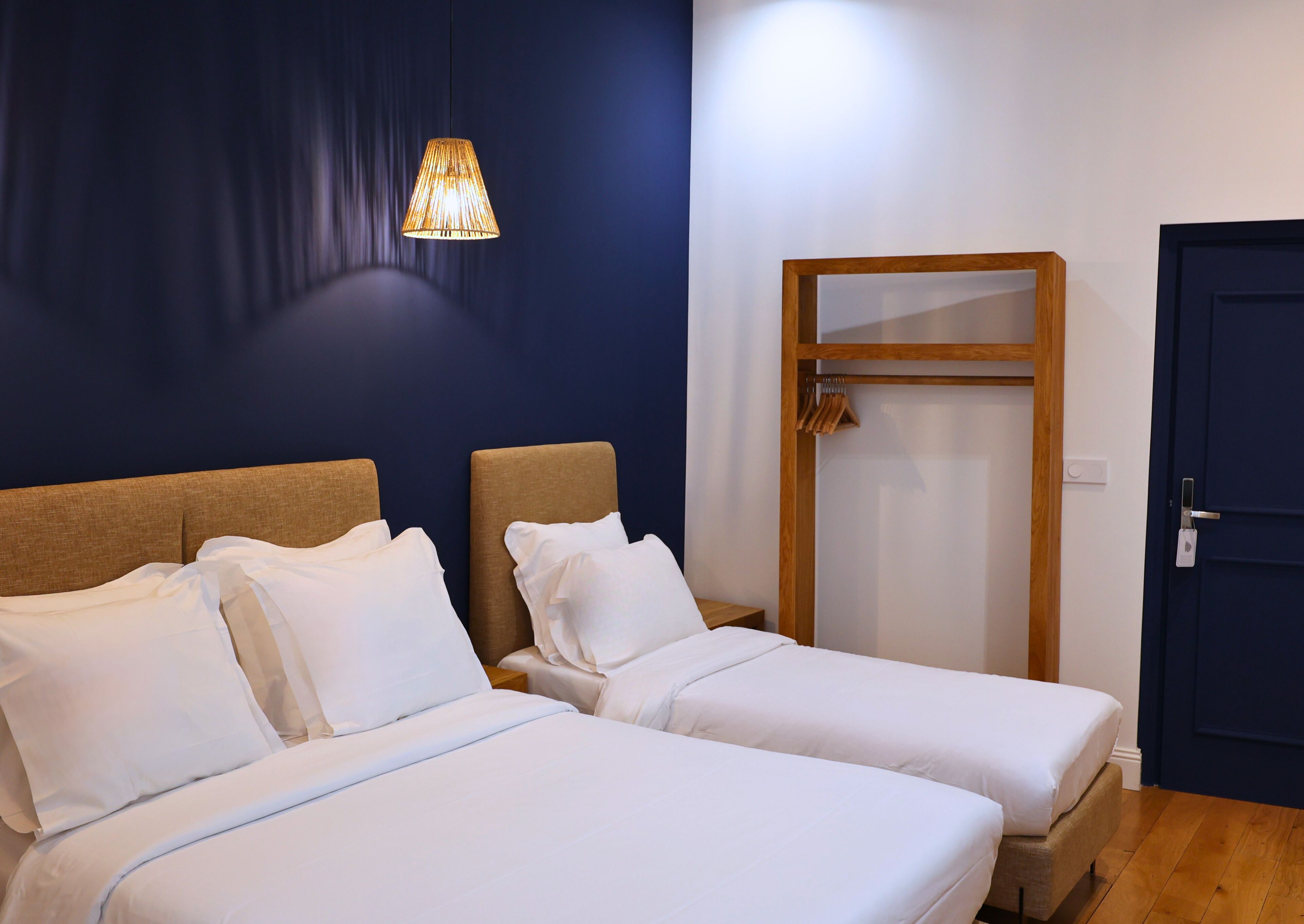 A hotel room with two beds, a hanging light fixture, a wooden wardrobe, and a door.