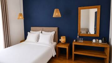 Une chambre d’hôtel comprenant un lit, une table de chevet, une lampe, un miroir et une petite table en bois.