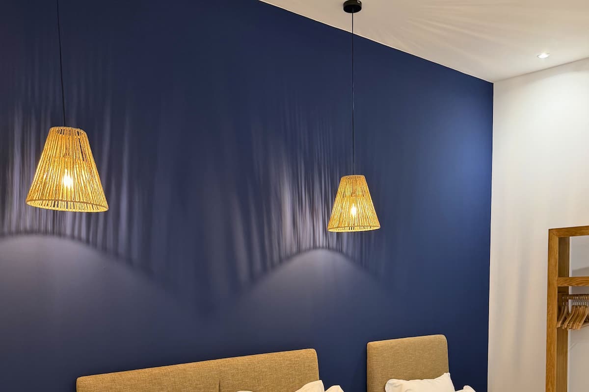 Une chambre d’hôtel avec deux lits, des têtes de lit en bois, du linge de lit blanc et deux lampes suspendues.