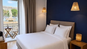 Habitación de hotel con cama, mesitas de noche, vista a una estatua en el exterior y un balcón con mesa y sillas.