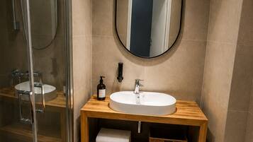 Un baño moderno con cabina de ducha de vidrio, tocador de madera con espejo redondo, lavabo blanco y un inodoro.