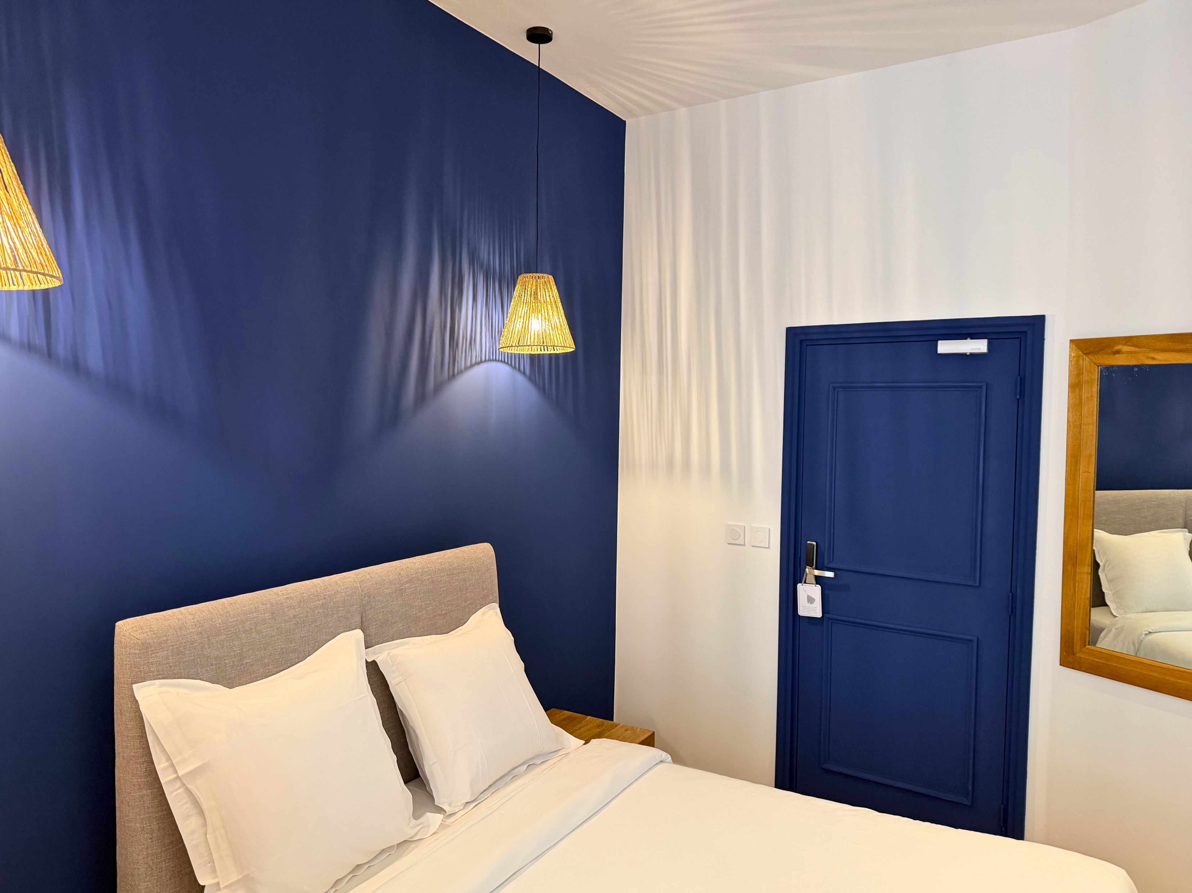 Una habitació d'hotel amb un llit, una porta blava i una làmpada penjant.