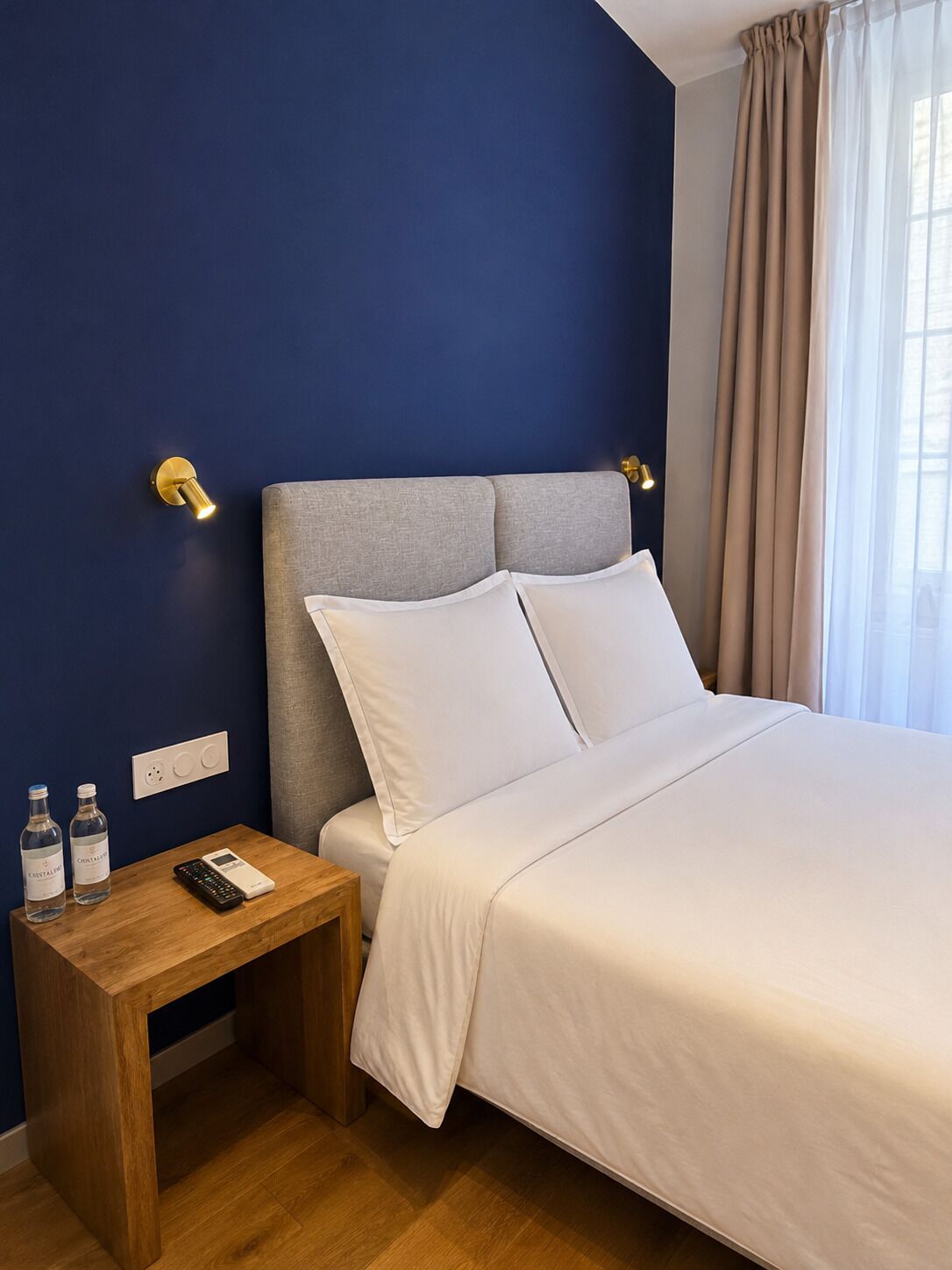 Quarto de hotel com cama, mesa de cabeceira e uma tomada na parede.
