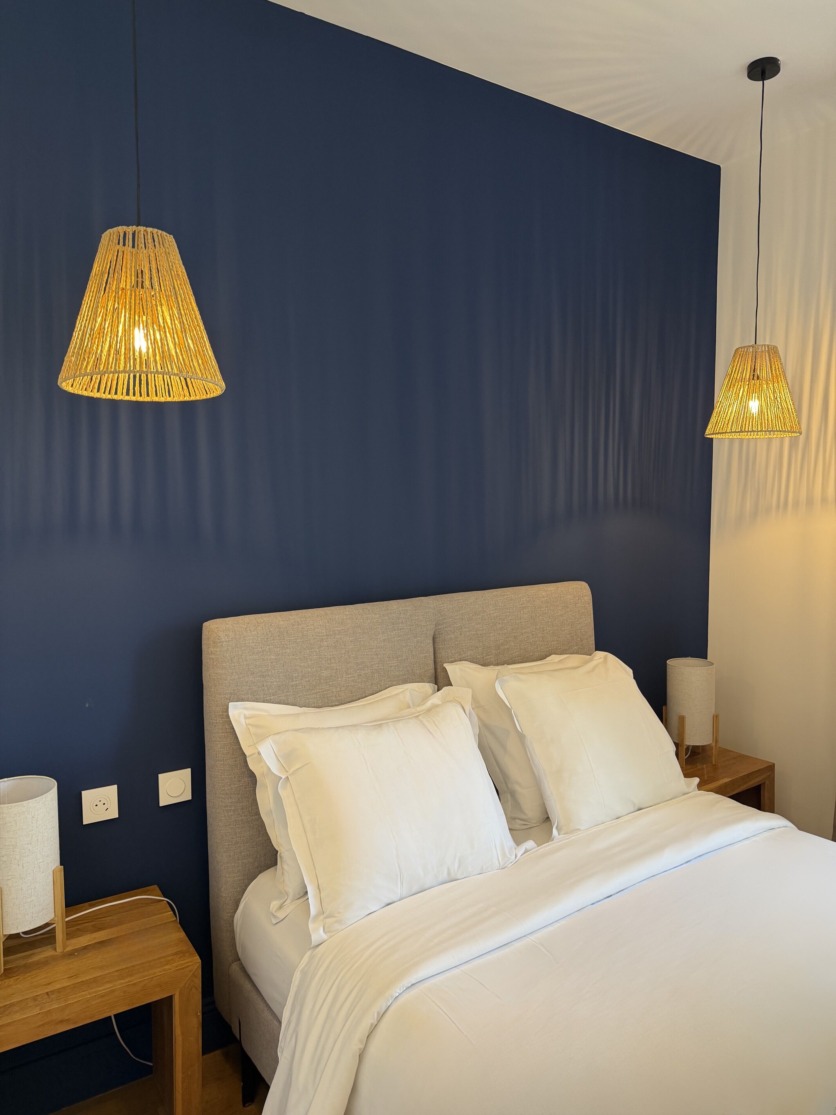 A bedroom with a bed, two bedside tables, and two hanging lamps.
