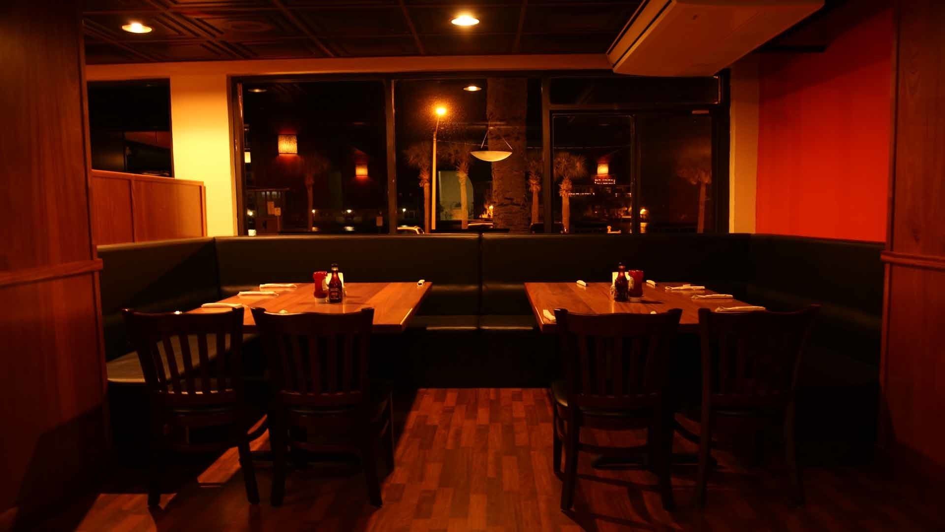 A dimly lit restaurant with wooden tables and booths, a warm ambiance, and a view through large windows.