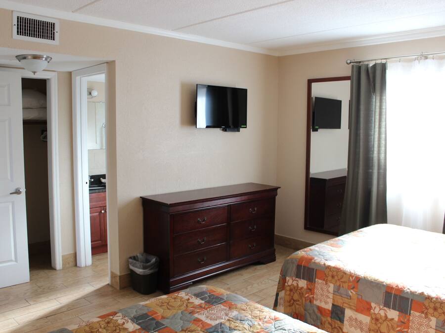 A bedroom with two beds, a dresser, a television, and a bathroom door.