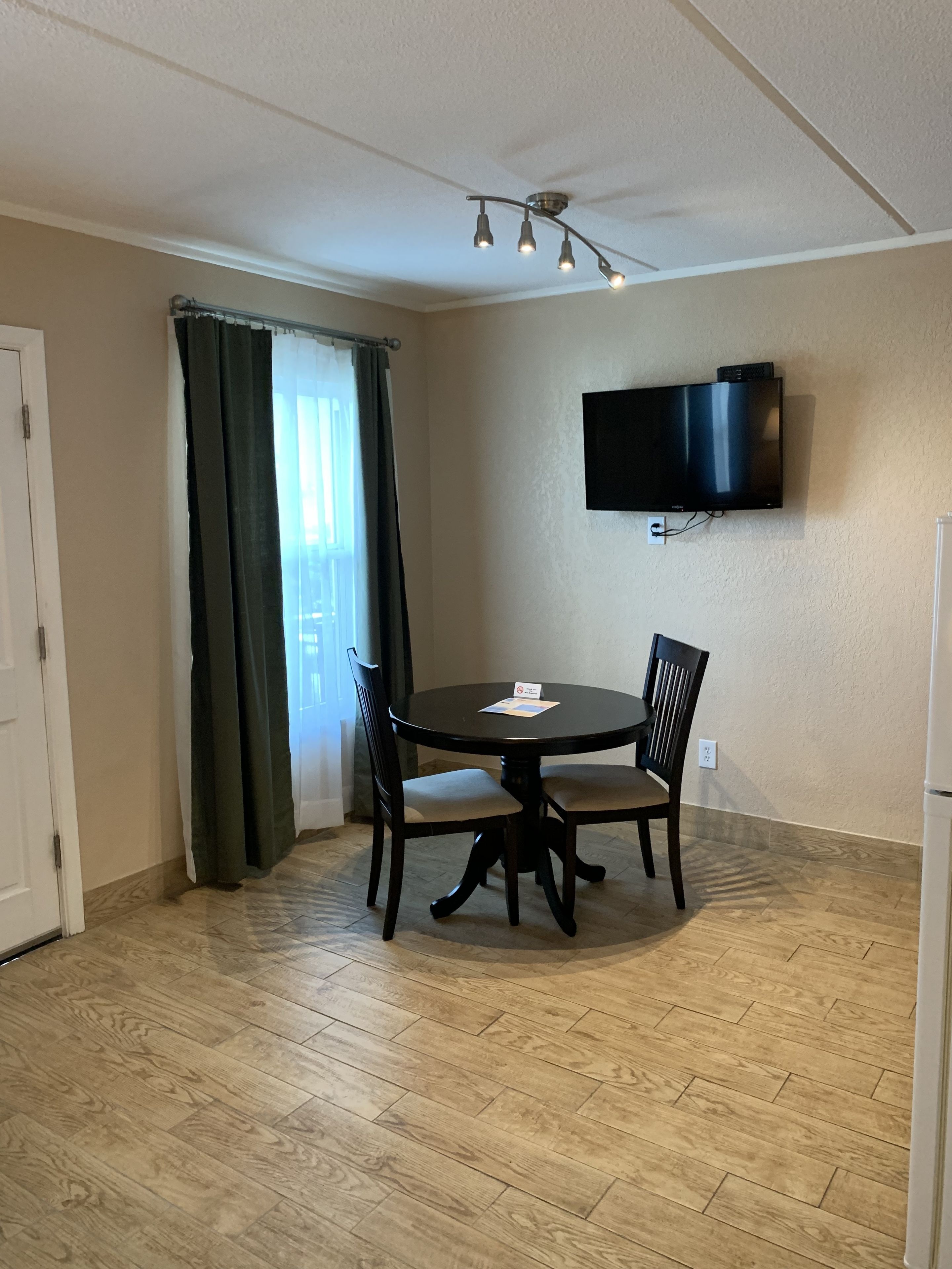 Quarto pequeno com mesa de jantar, cadeiras, televisão de tela plana na parede e janela com cortinas.