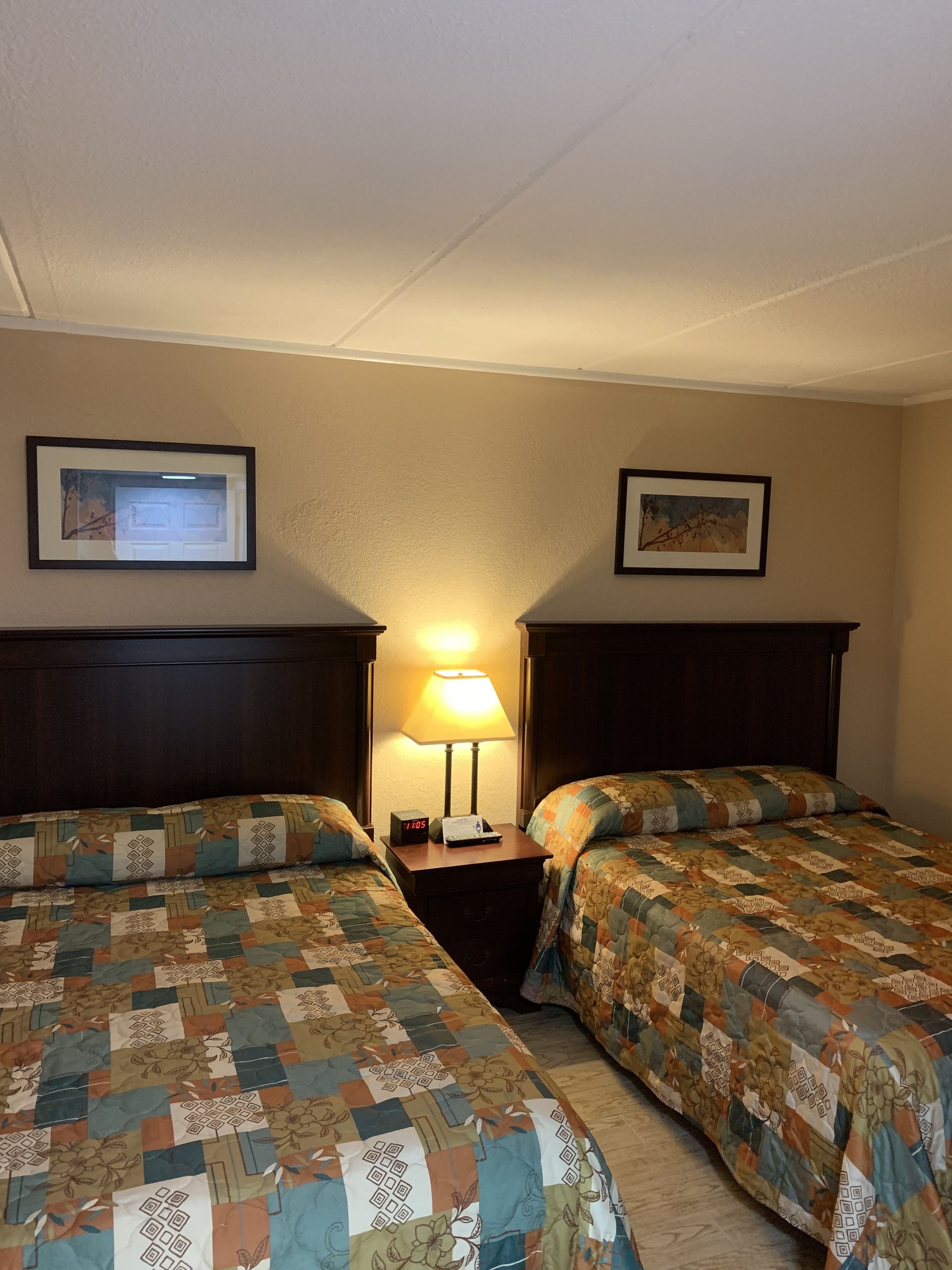 A hotel room with two beds, a nightstand with a lamp, and framed pictures on the walls.