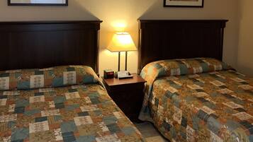A hotel room with two beds, a nightstand with a lamp, and framed pictures on the walls.