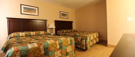 A hotel room with two beds, wooden headboards, and a nightstand with a lamp.
