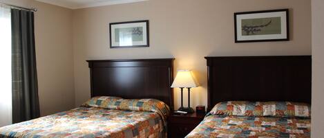 A hotel room with two beds, a nightstand, a lamp, and two framed pictures on the wall.