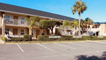 A motel with a parking lot, a covered walkway, and a palm tree.