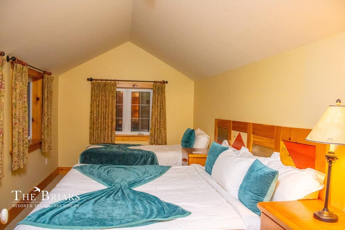 A hotel room with two beds, a window with curtains, a lamp, and a wooden headboard.