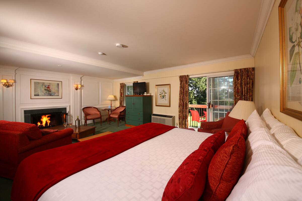 A hotel room with a large bed, a fireplace, a desk, and a view of the outdoors.