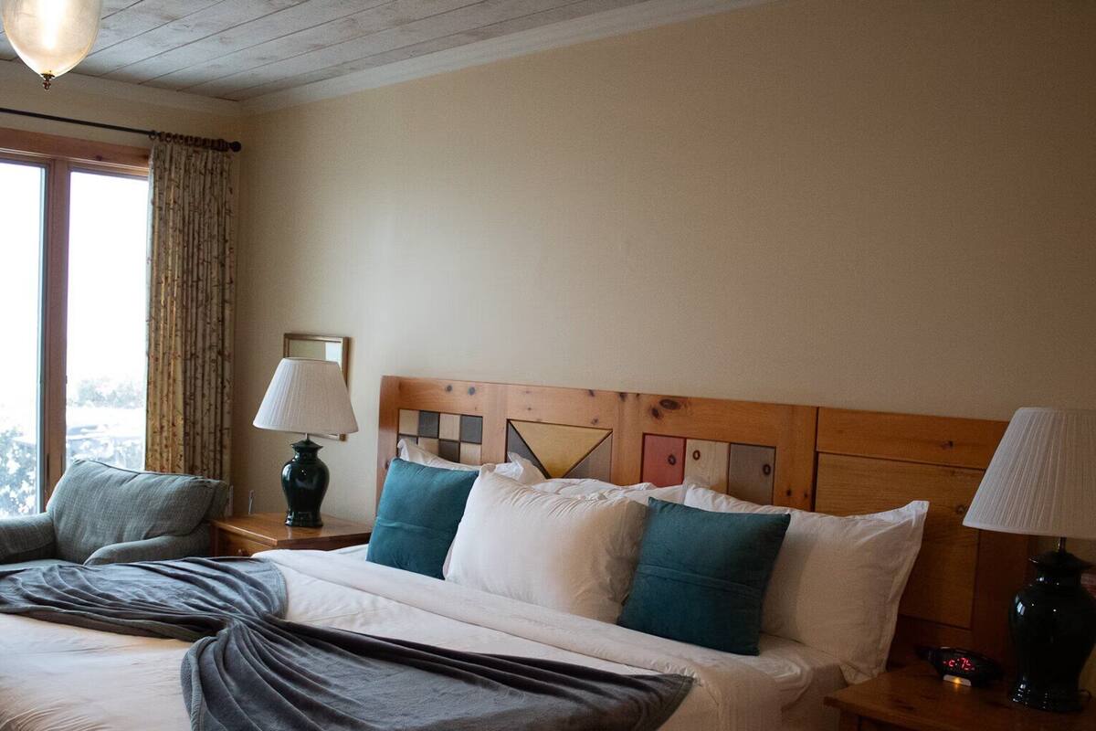 A hotel room with a large bed, two bedside tables, a lamp, and a view through the window.