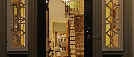 A dark wooden door with intricate glass panels and a chandelier inside.
