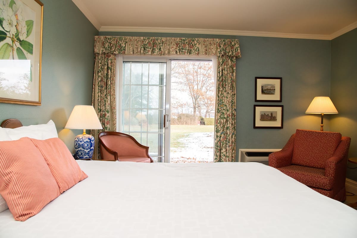 A hotel room with a large bed, two chairs, a table, and a window with curtains.