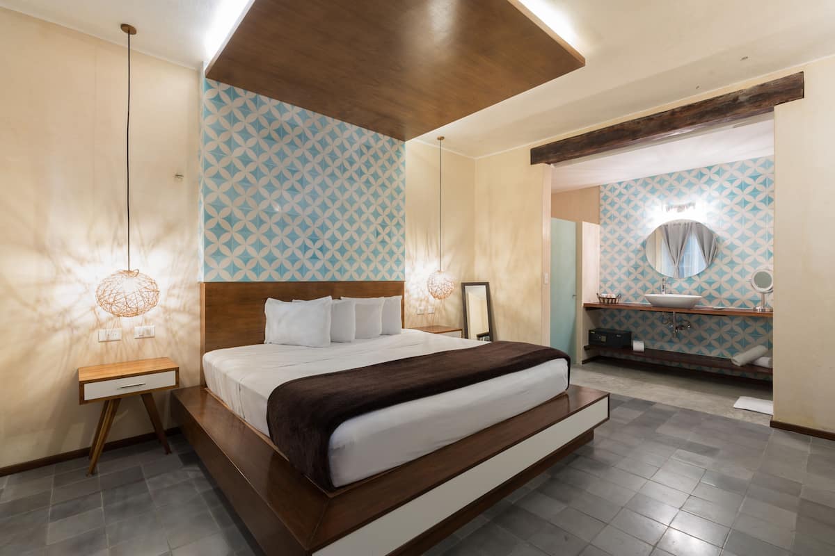 Een moderne slaapkamer met een groot bed, nachtlampjes en een badkamer met een wastafel en spiegel.