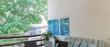 Una terraza de madera con mobiliario de mimbre, un sofá a rayas y un ordenador portátil sobre una mesa.