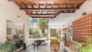 A spacious interior with a wooden ceiling, a seating area with cushions, and a wall with a grid pattern.