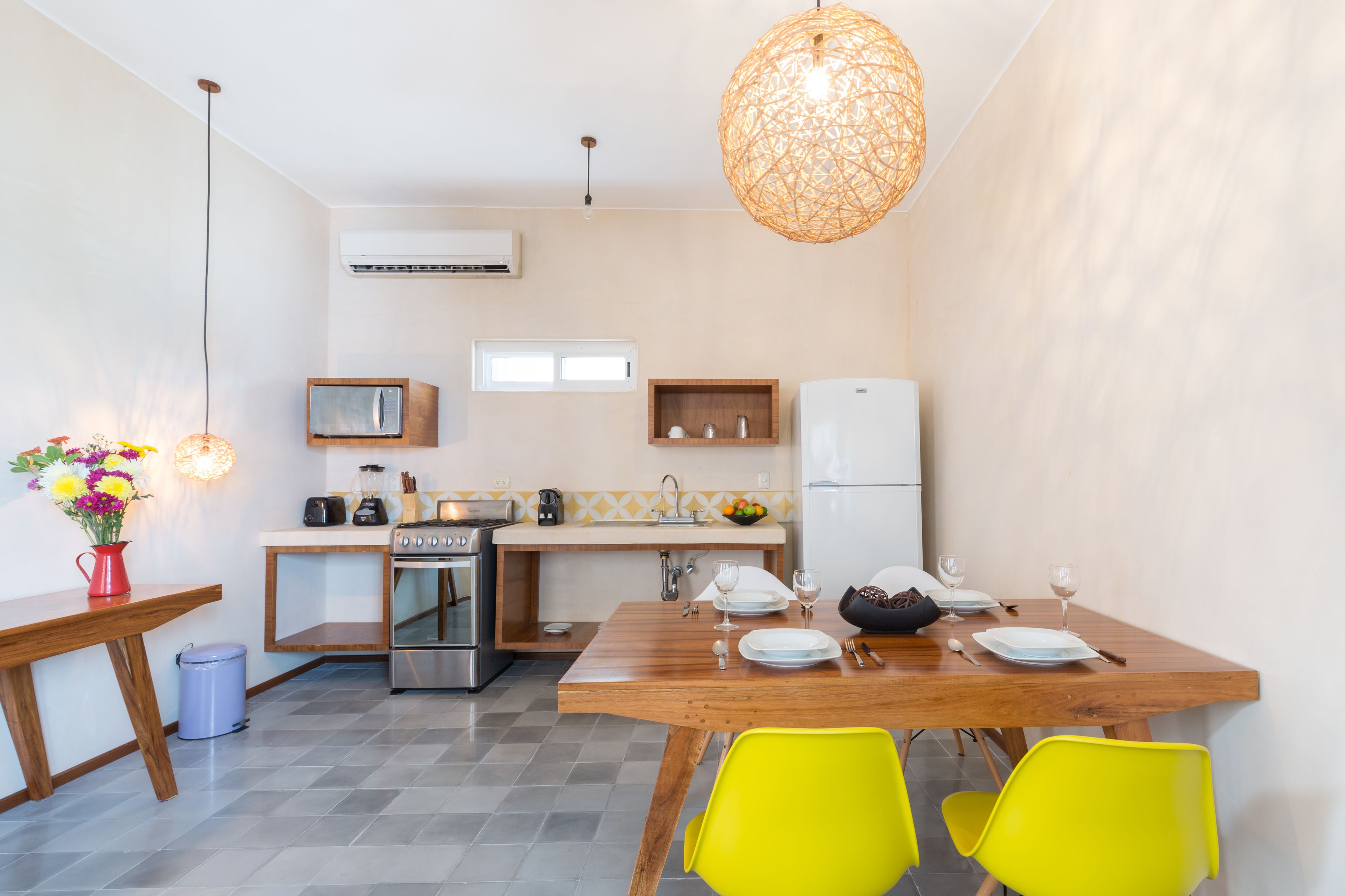 A compact kitchen with modern appliances, a dining area with yellow chairs, and a hanging light fixture.