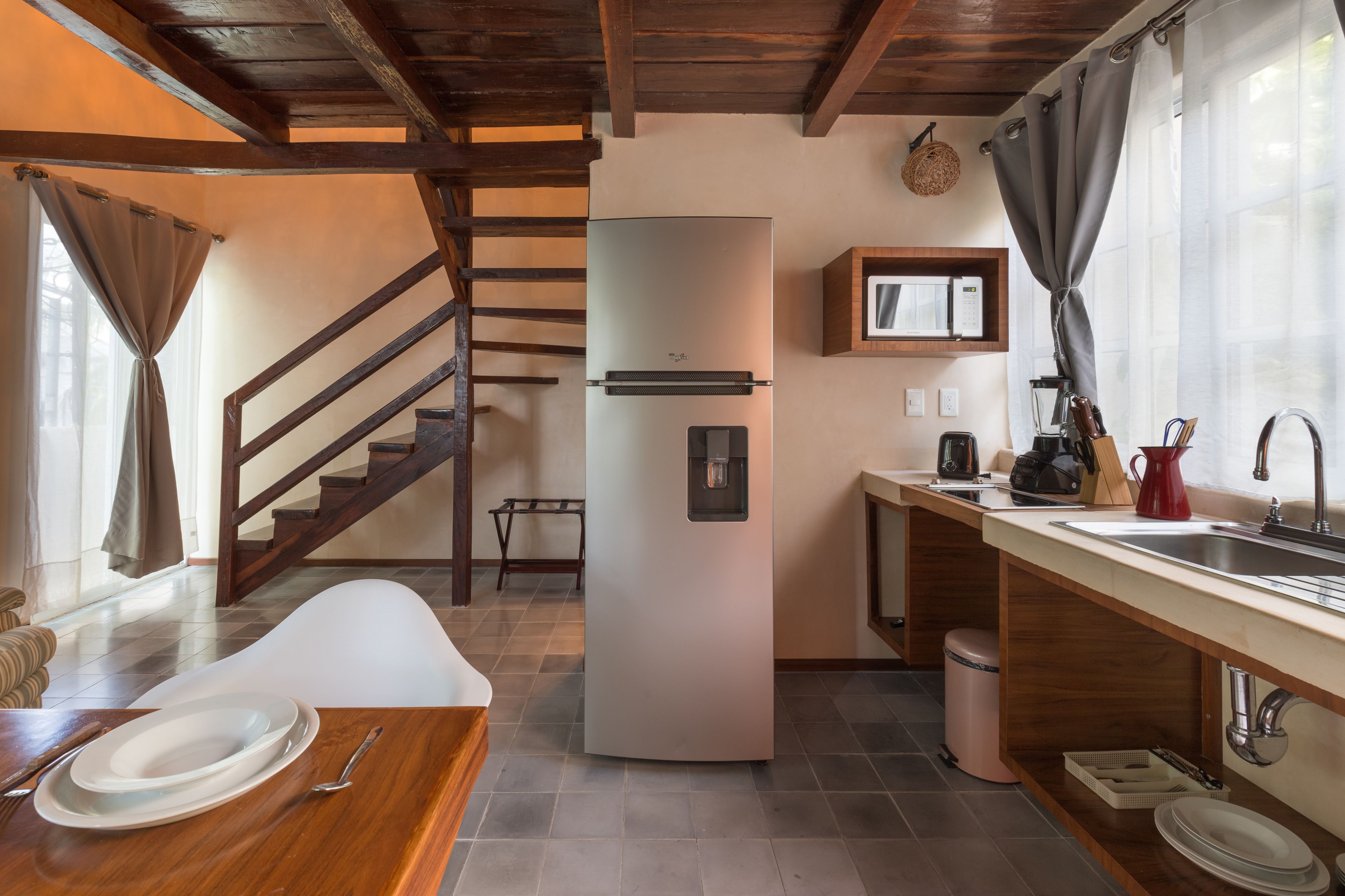 Une cuisine équipée d’un réfrigérateur, d’un évier et d’un comptoir en bois. Un escalier mène à un autre niveau.