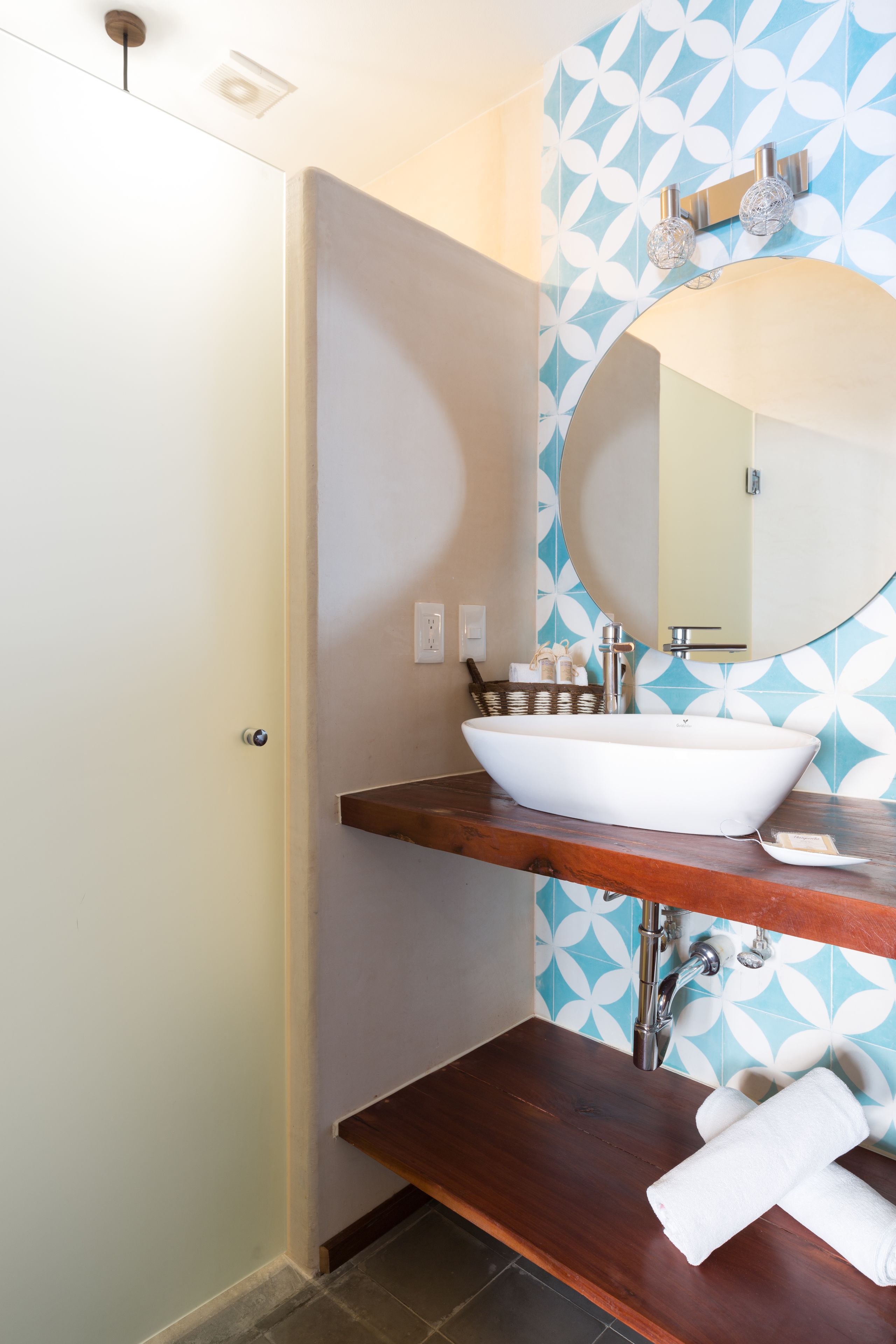 Un baño con un lavamanos blanco tipo recipiente, un mueble de tocador de madera, un espejo y un papel tapiz estampado.