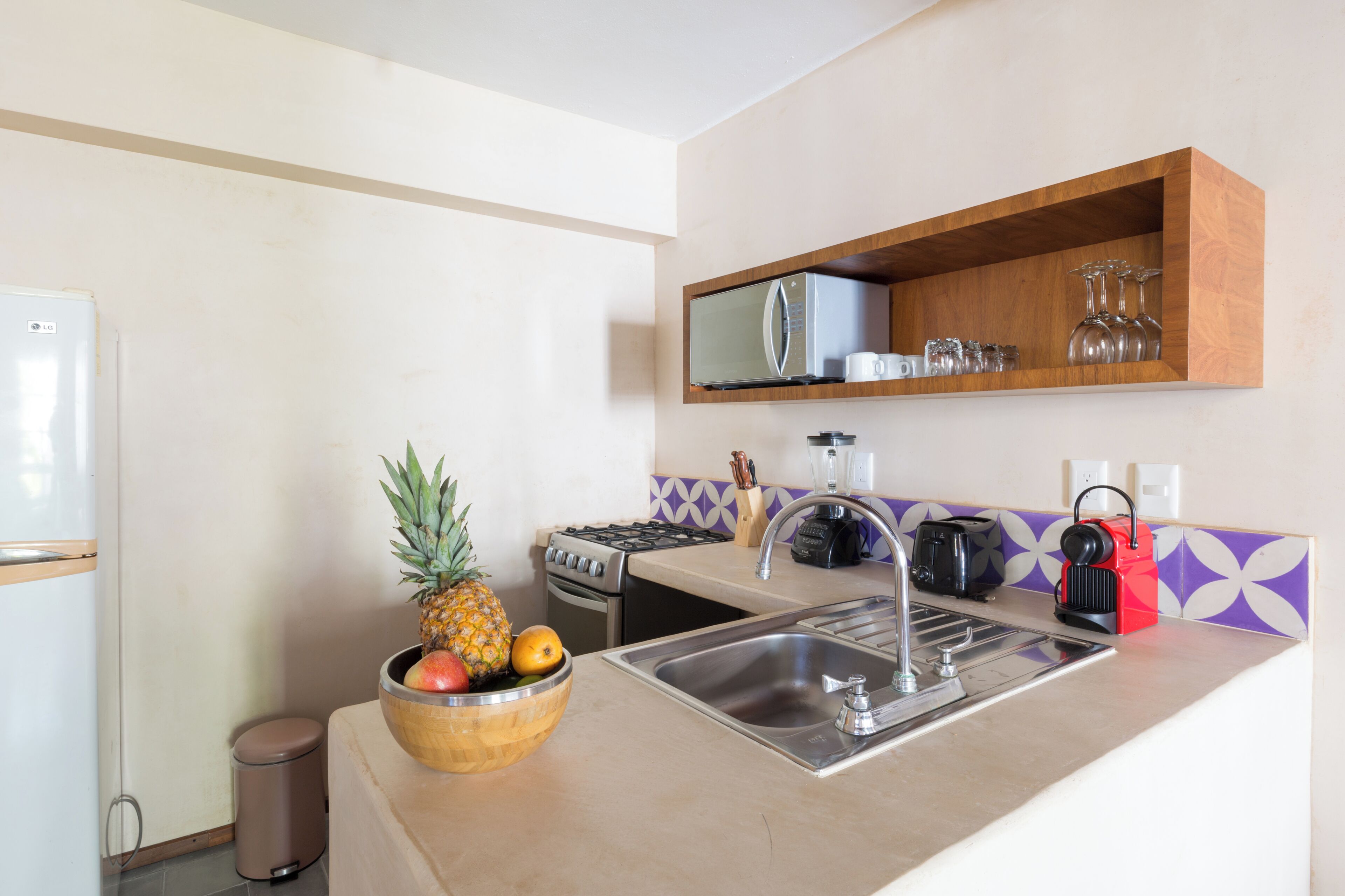 A kitchen with a refrigerator, stove, sink, and a fruit bowl.