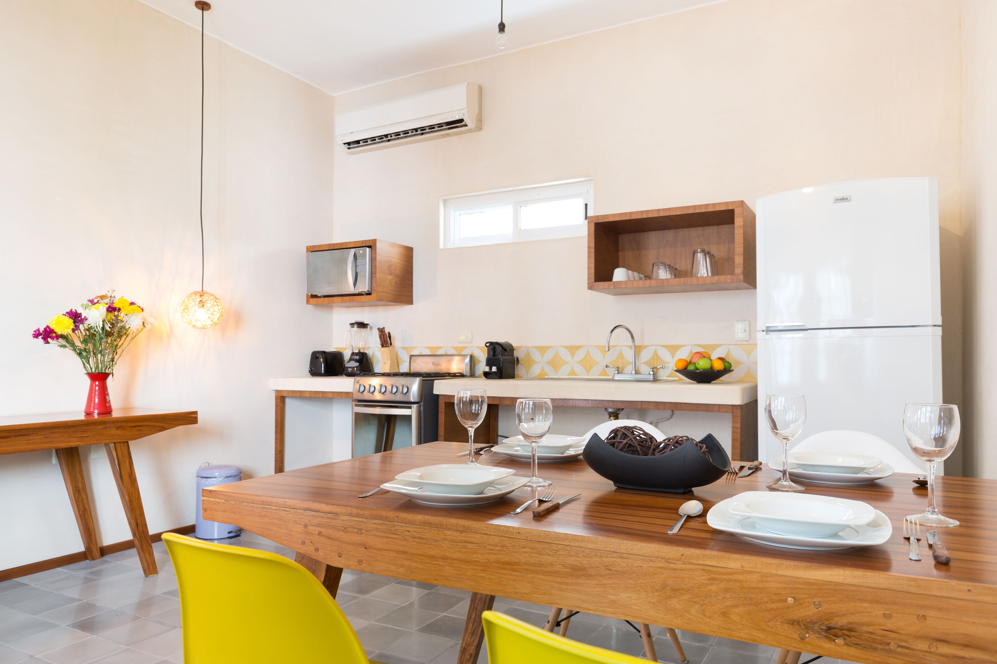 A modern kitchen with a wooden dining table set for two, a built-in oven, and a refrigerator.