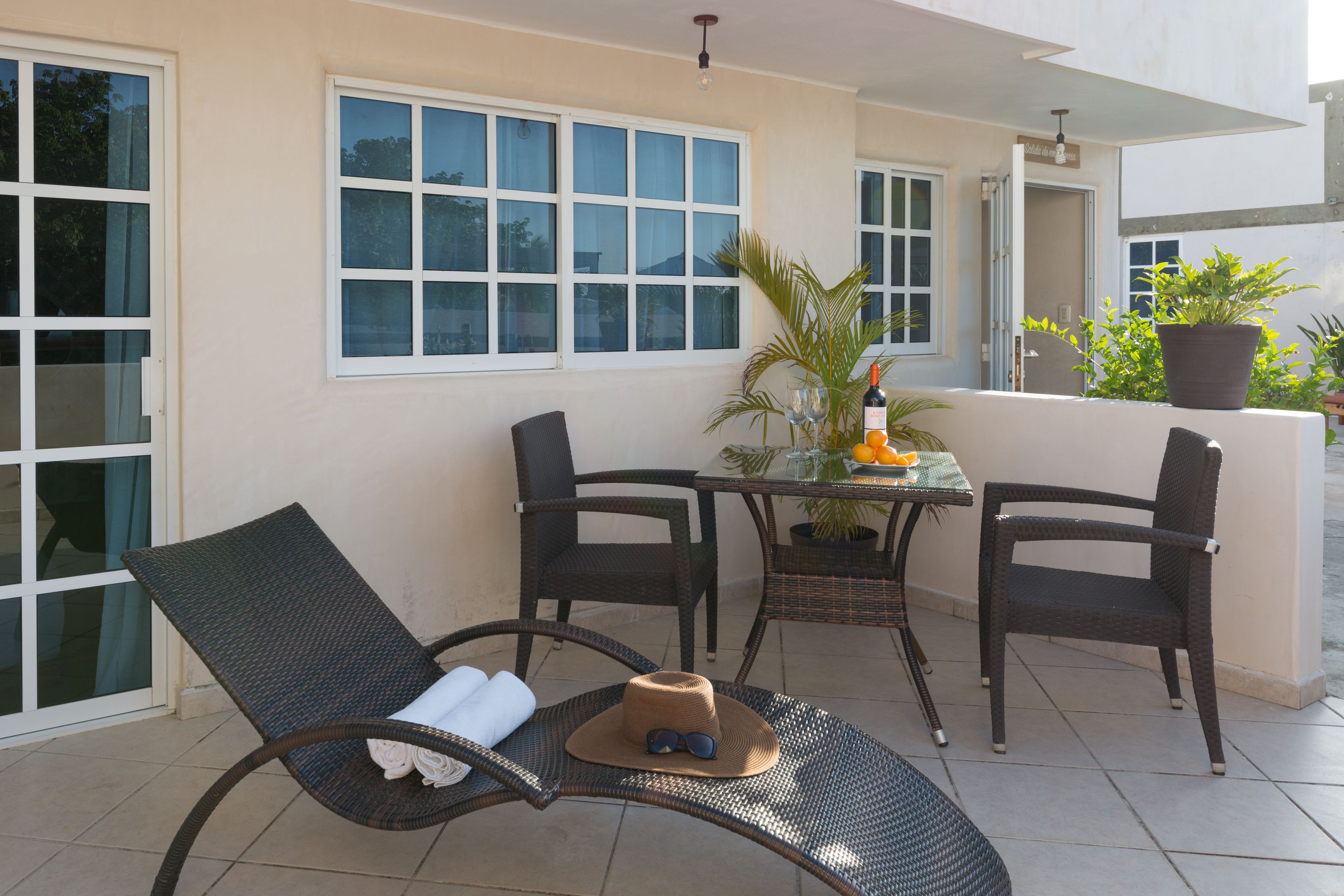 A patio with two wicker chairs, a table with a potted plant, and a bottle of wine.