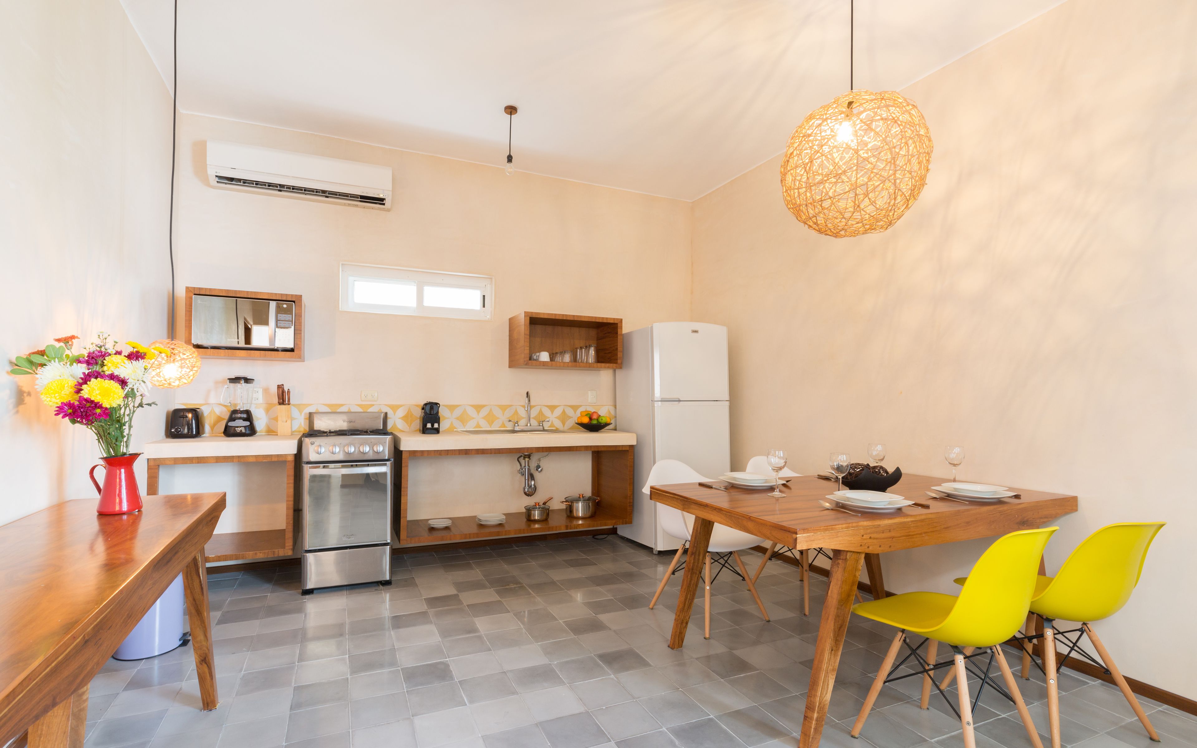A compact kitchen with a stove, sink, and refrigerator. There is a dining table with chairs and a vase of flowers.