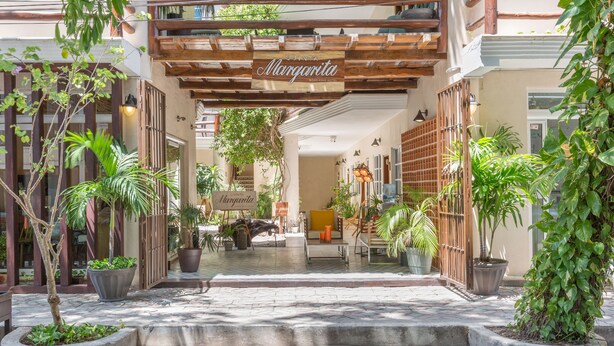 A hotel entrance with a wooden pergola, potted plants, and a sign reading "Quinta Margarita".