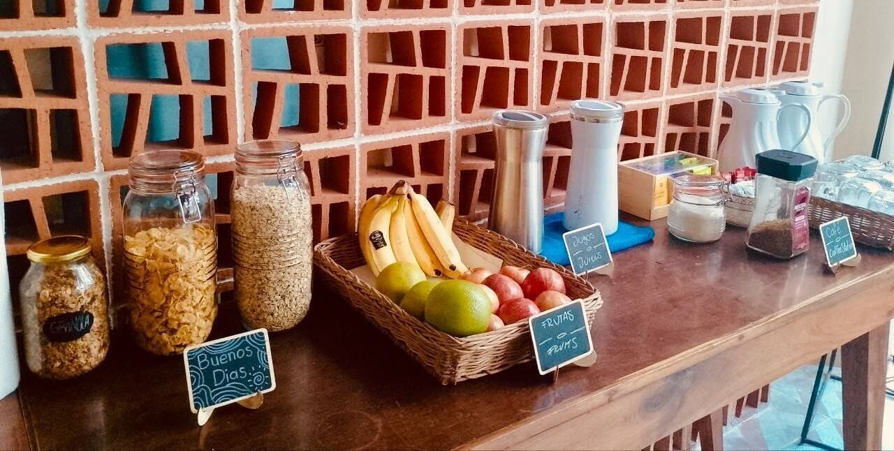 Una barra de desayuno con diversos alimentos y recipientes, incluyendo tarros de granola y una cesta de frutas.