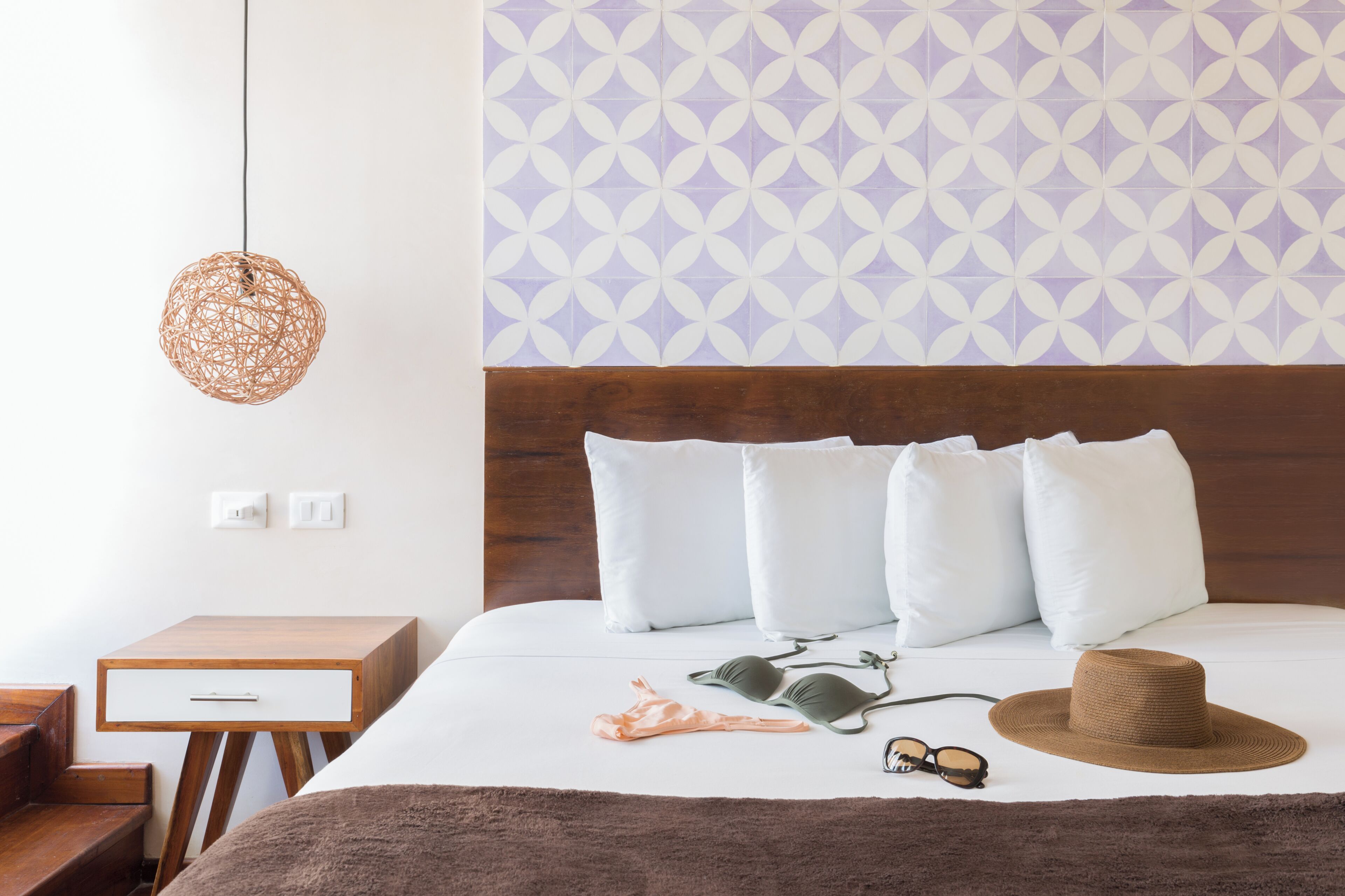 Una cama bien hecha con almohadas blancas, un sombrero marrón y gafas de sol.