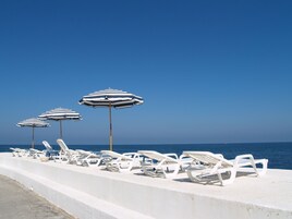A beachside lounge with white lounge chairs and striped umbrellas, overlooking the sea.