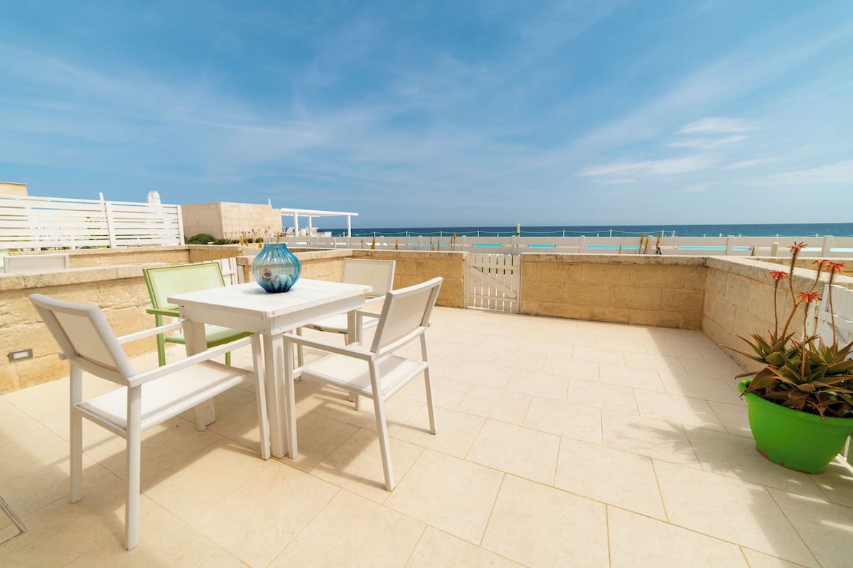 A terrace with a table and chairs, a potted plant, and a view of the beach.