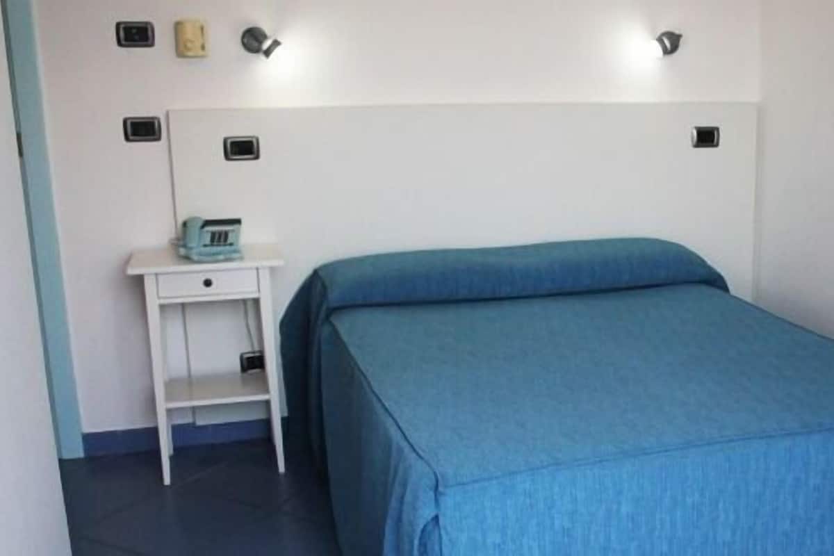 A single bed with a blue bedspread in a room with white walls and a white nightstand.